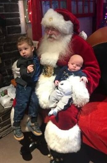 Two children sitting with Santa Claus during a festive event.